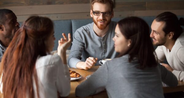 Diverse young people talking and having fun together in cafe, girls chatting sharing coffeehouse table with multiracial friends, multi-ethnic millennials enjoying pleasant discussion in public place